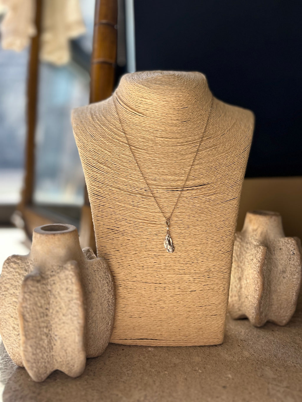 Necklace on a textured mannequin bust with decorative vases in the background