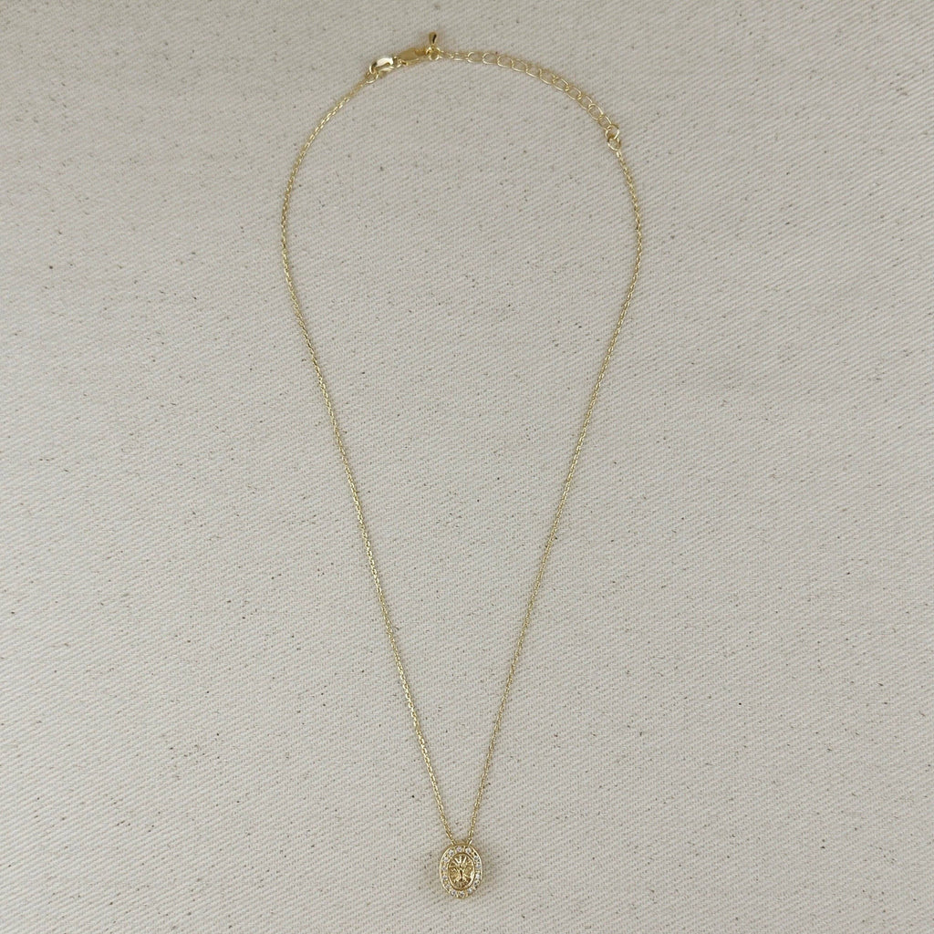 A delicate gold chain necklace with a small oval pendant, laid flat on a textured beige fabric background.