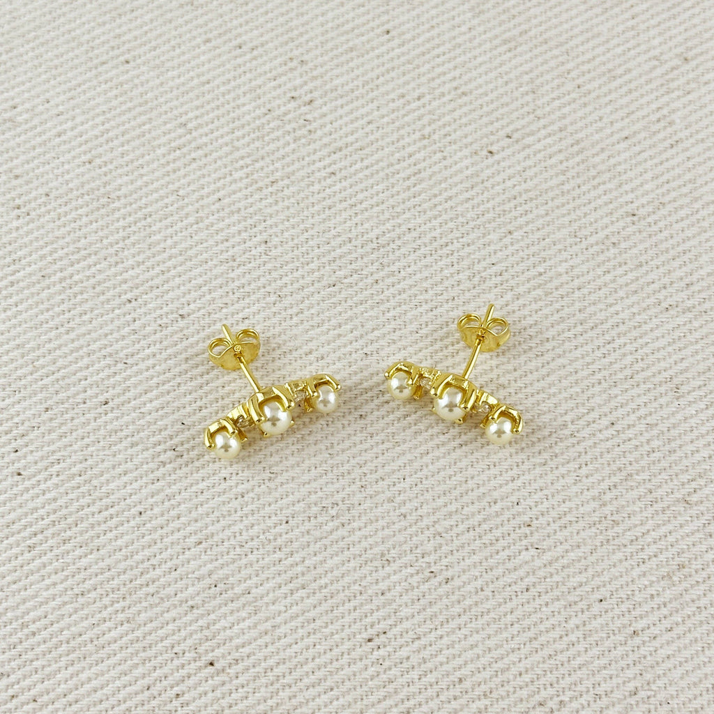 Pair of gold earrings with pearls on a beige fabric background