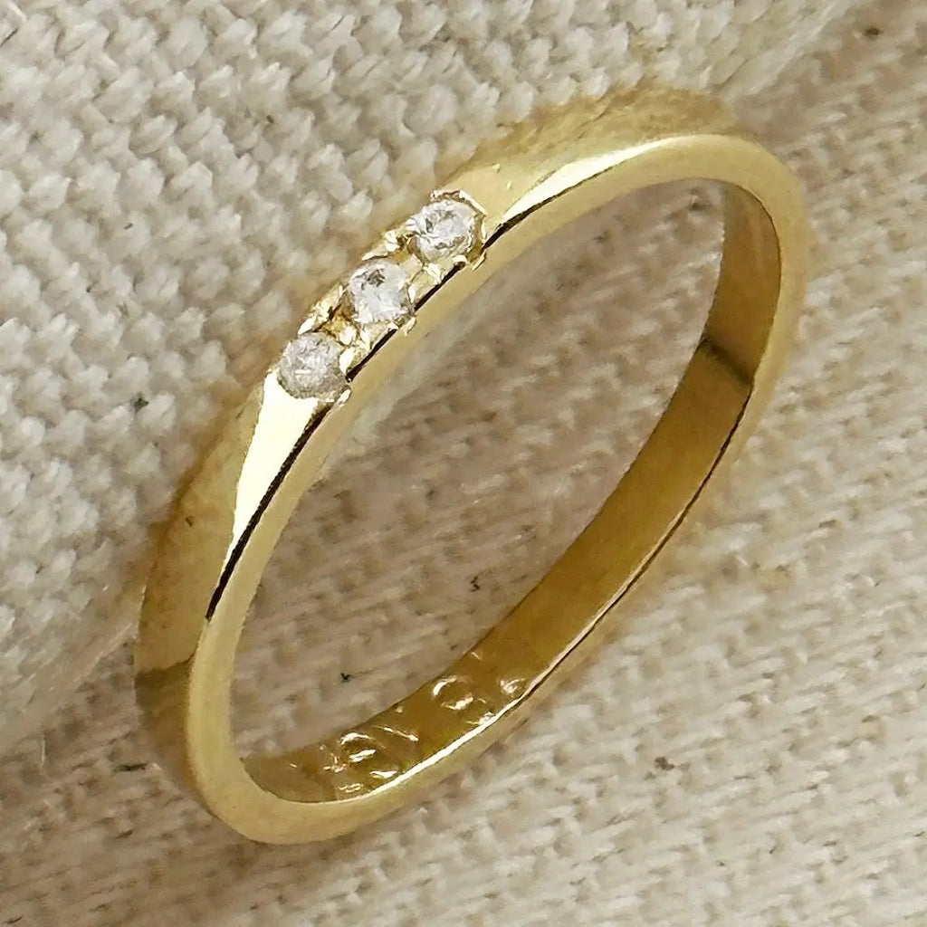 Gold ring with embedded diamonds on a textured beige surface