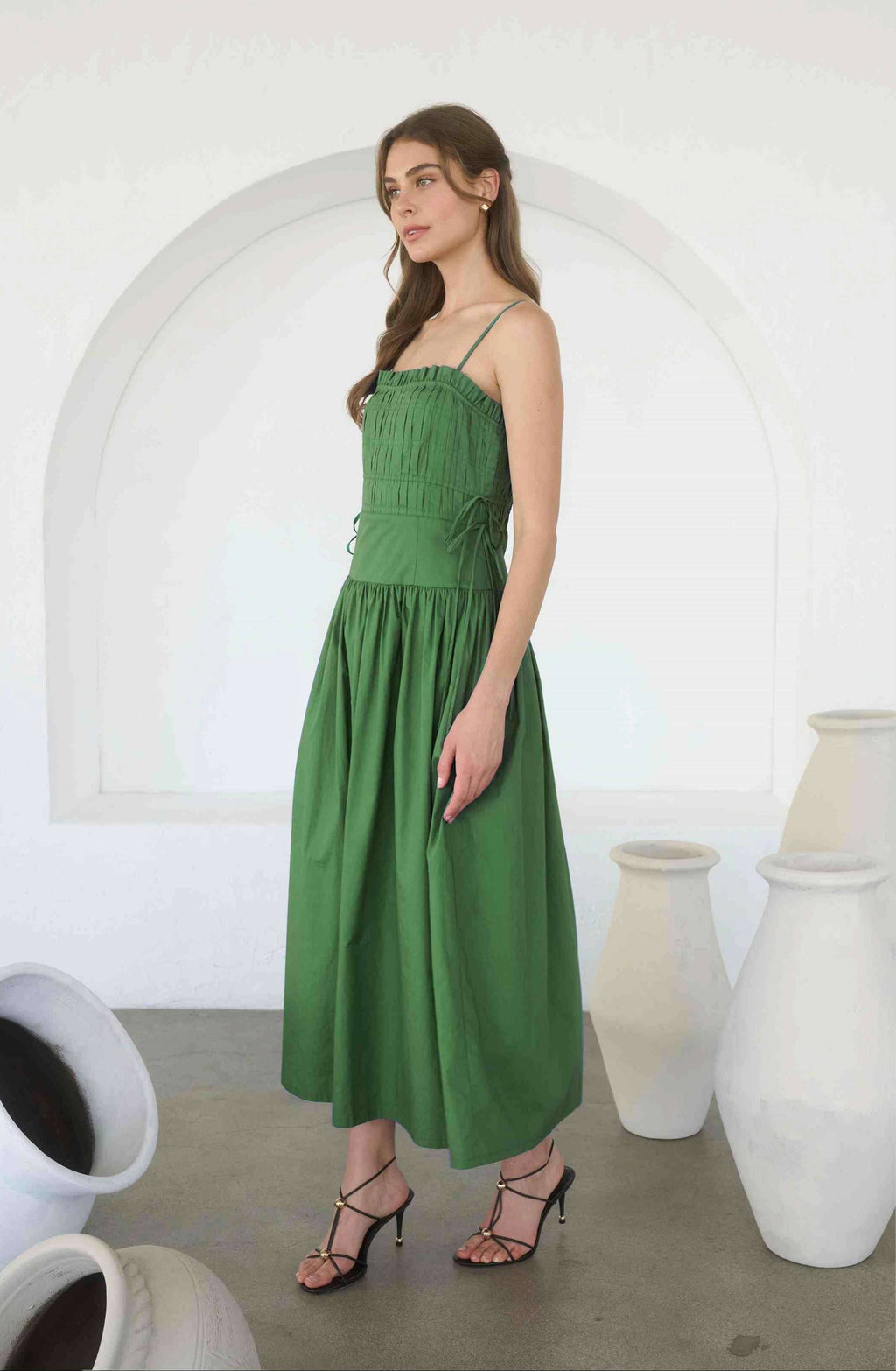 Woman wearing a green dress standing in a room with white arches and large vases.