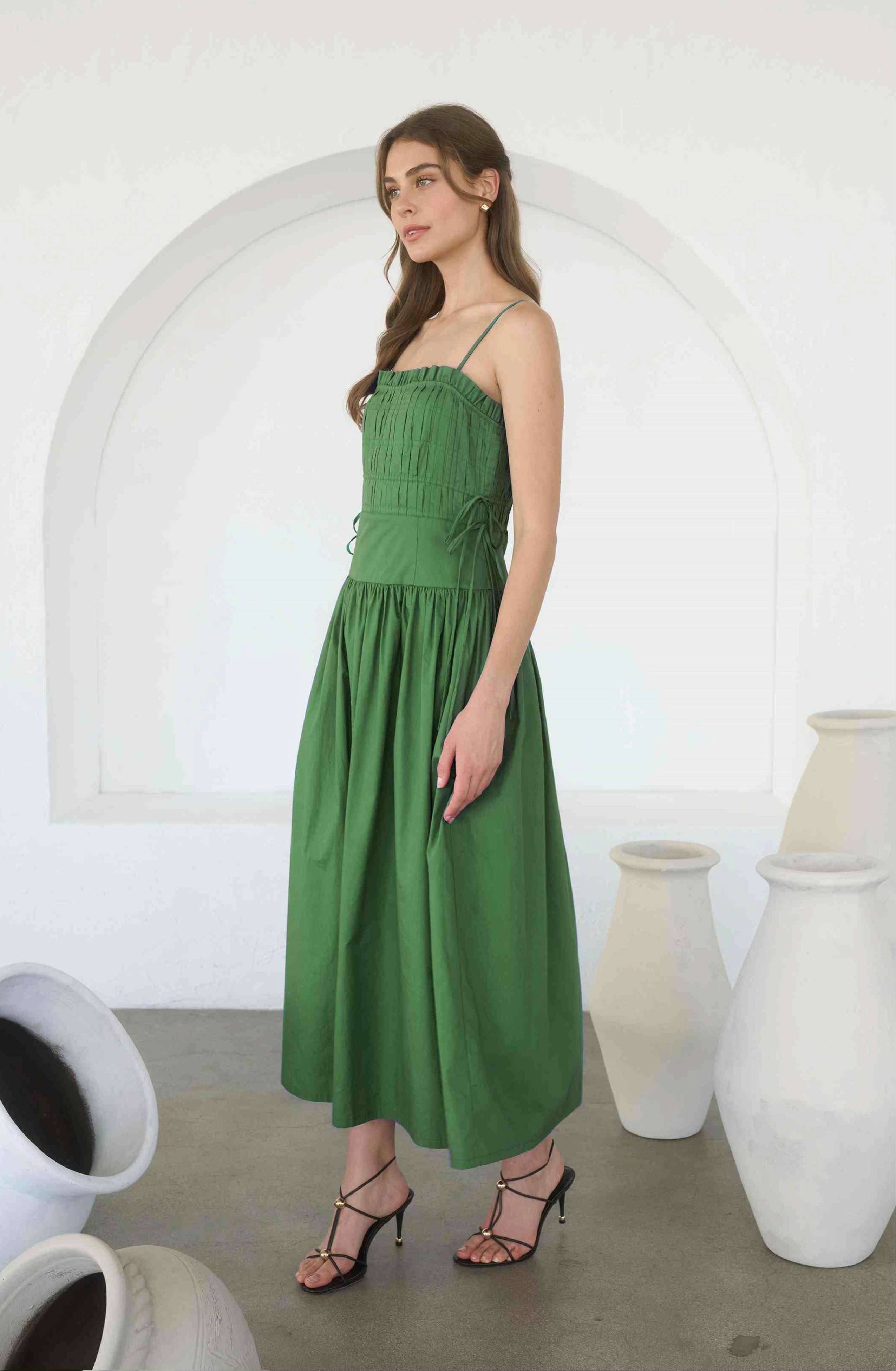 Woman wearing a green dress standing in a room with white arches and large vases.