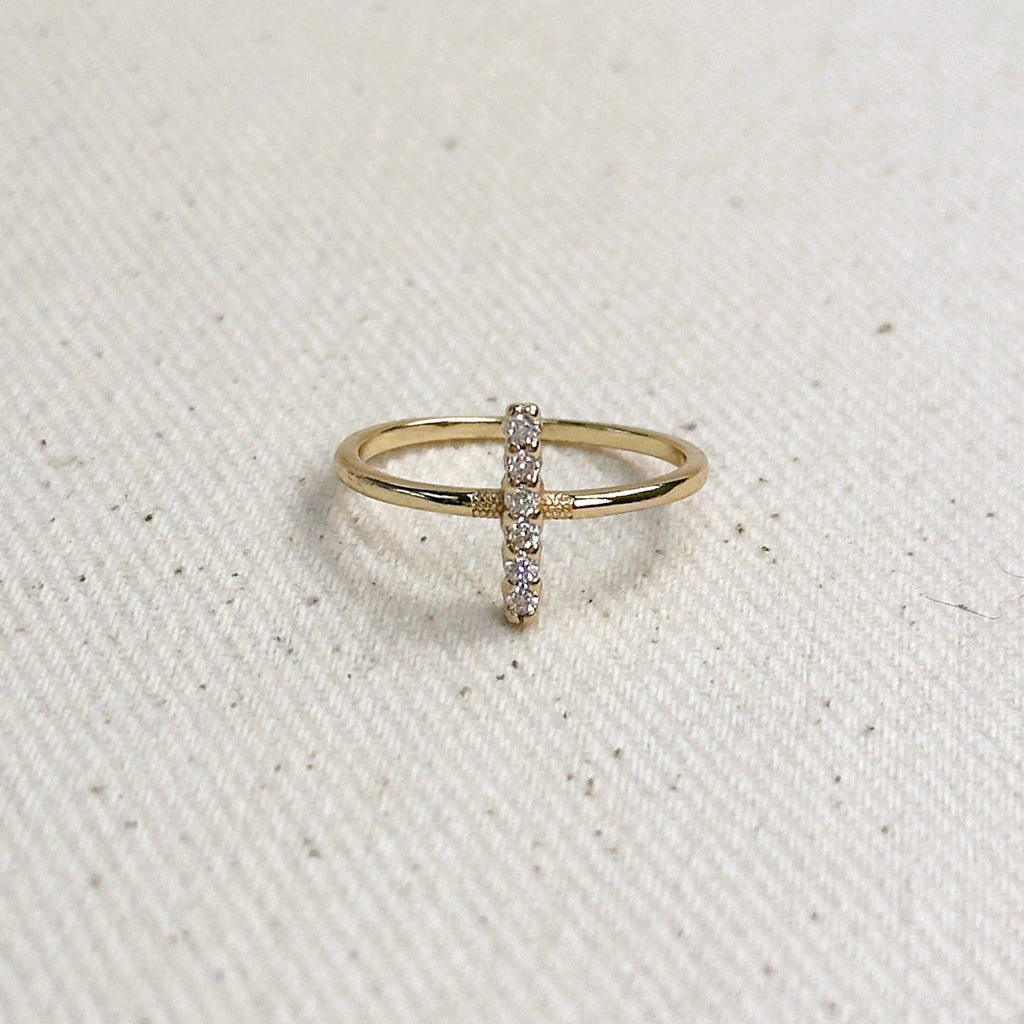 A delicate gold ring featuring a vertical bar studded with small clear stones, resting on a textured off-white fabric background.