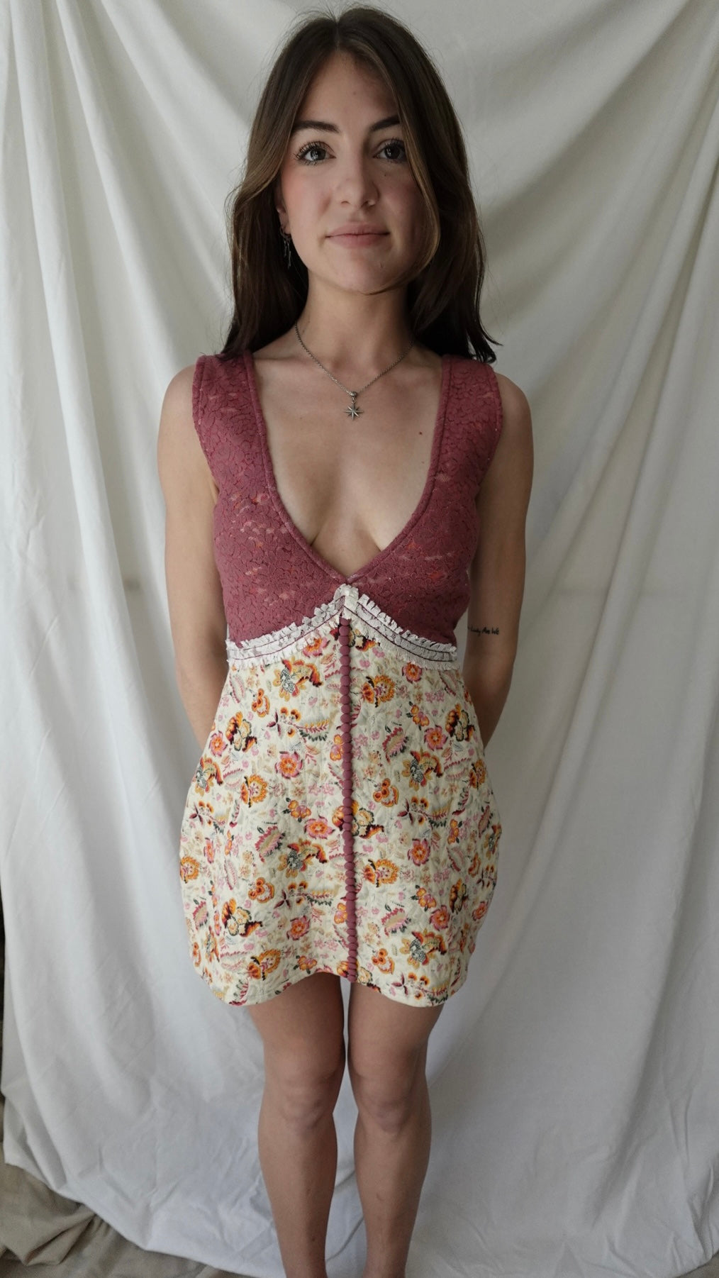 Woman wearing a floral dress with a maroon top against a white curtain background