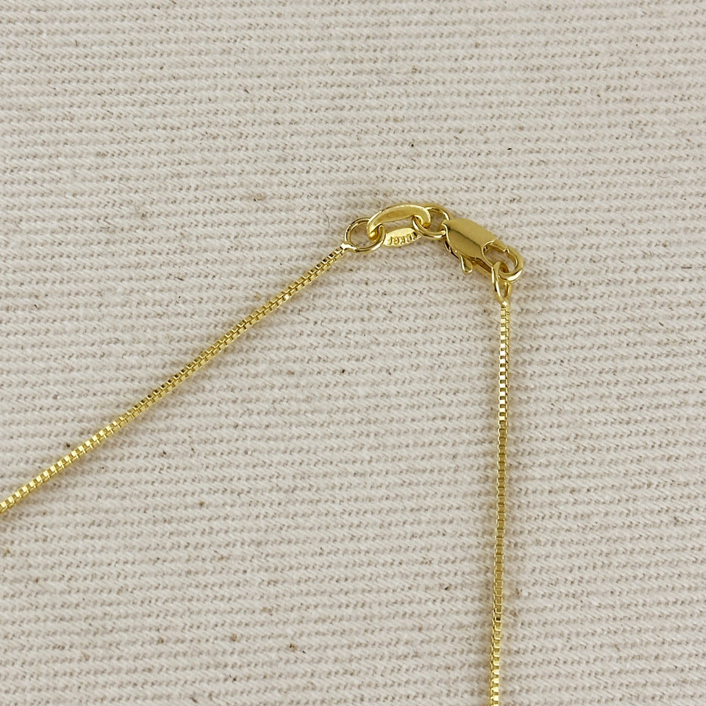 Close-up of a gold chain necklace clasp and extender on a textured beige fabric background.