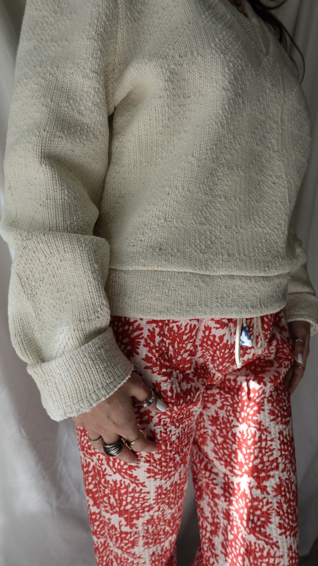 Person wearing a beige sweater and red patterned pants on a white surface