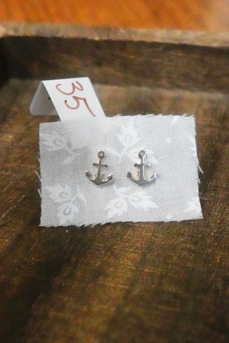 Anchor-shaped earrings on a white card with a number tag, placed on a wooden surface.