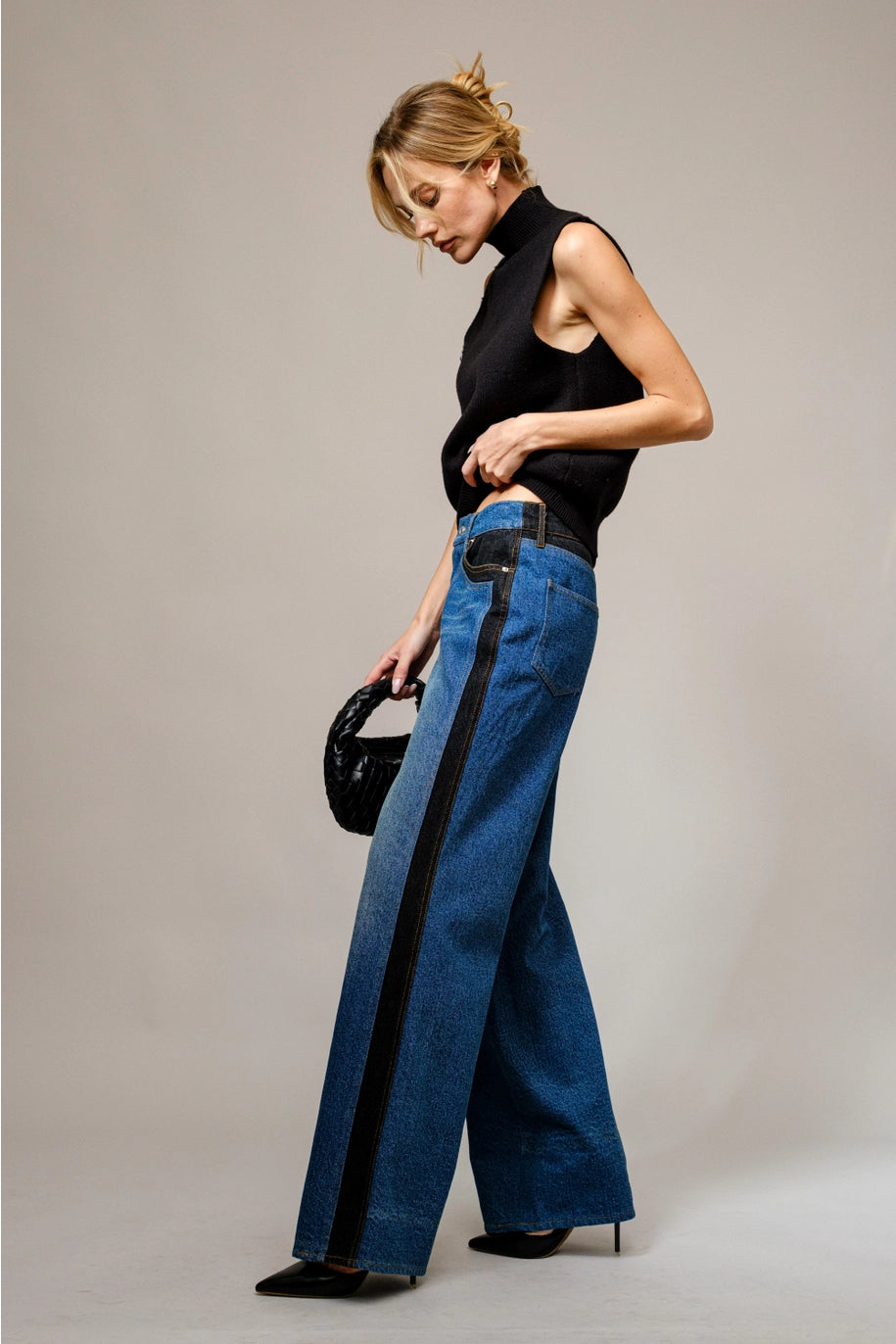 Woman wearing blue jeans with black accents and a black top against a neutral background