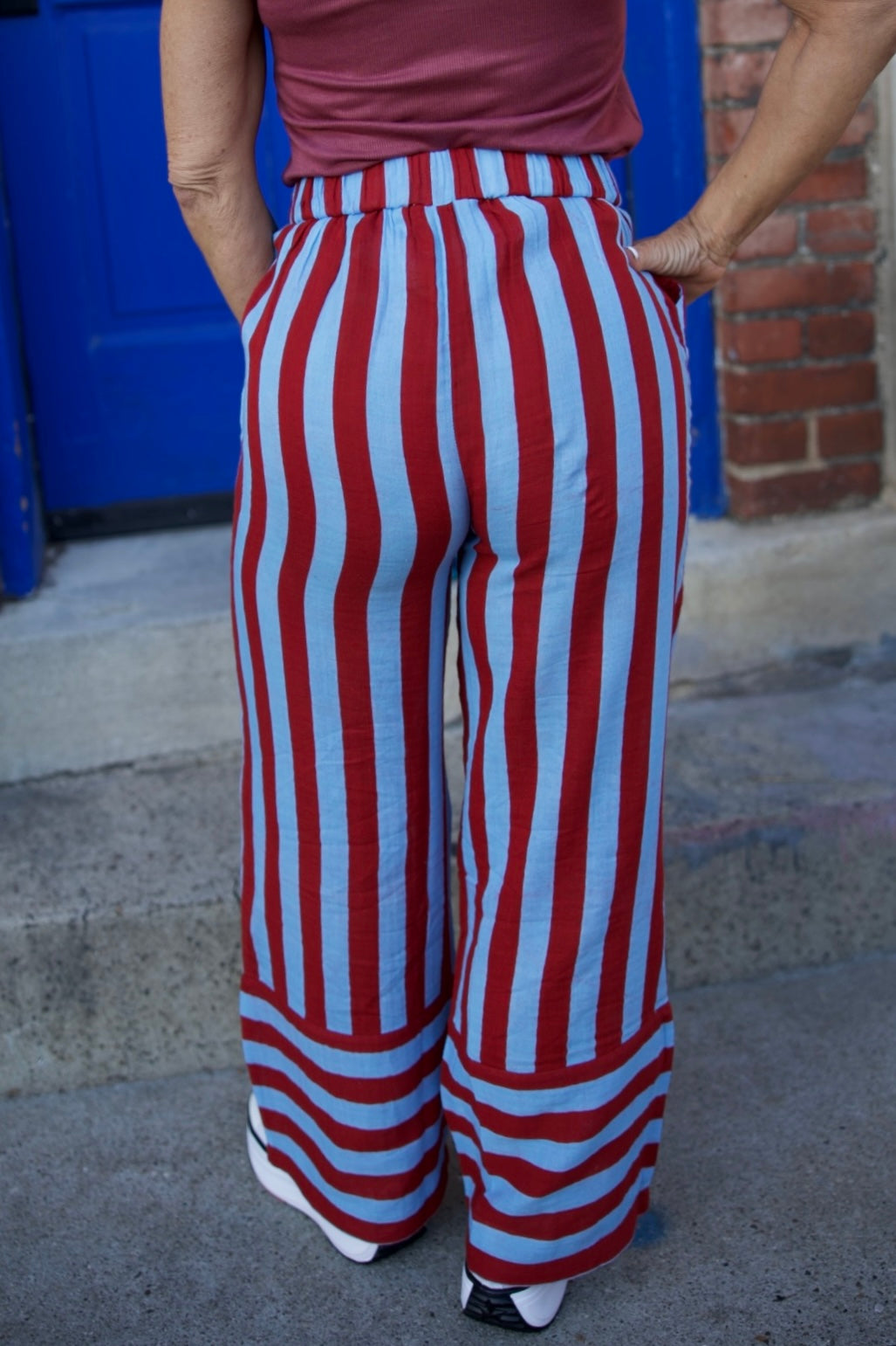 Person wearing red and white striped pants with a blue door and brick wall in the background
