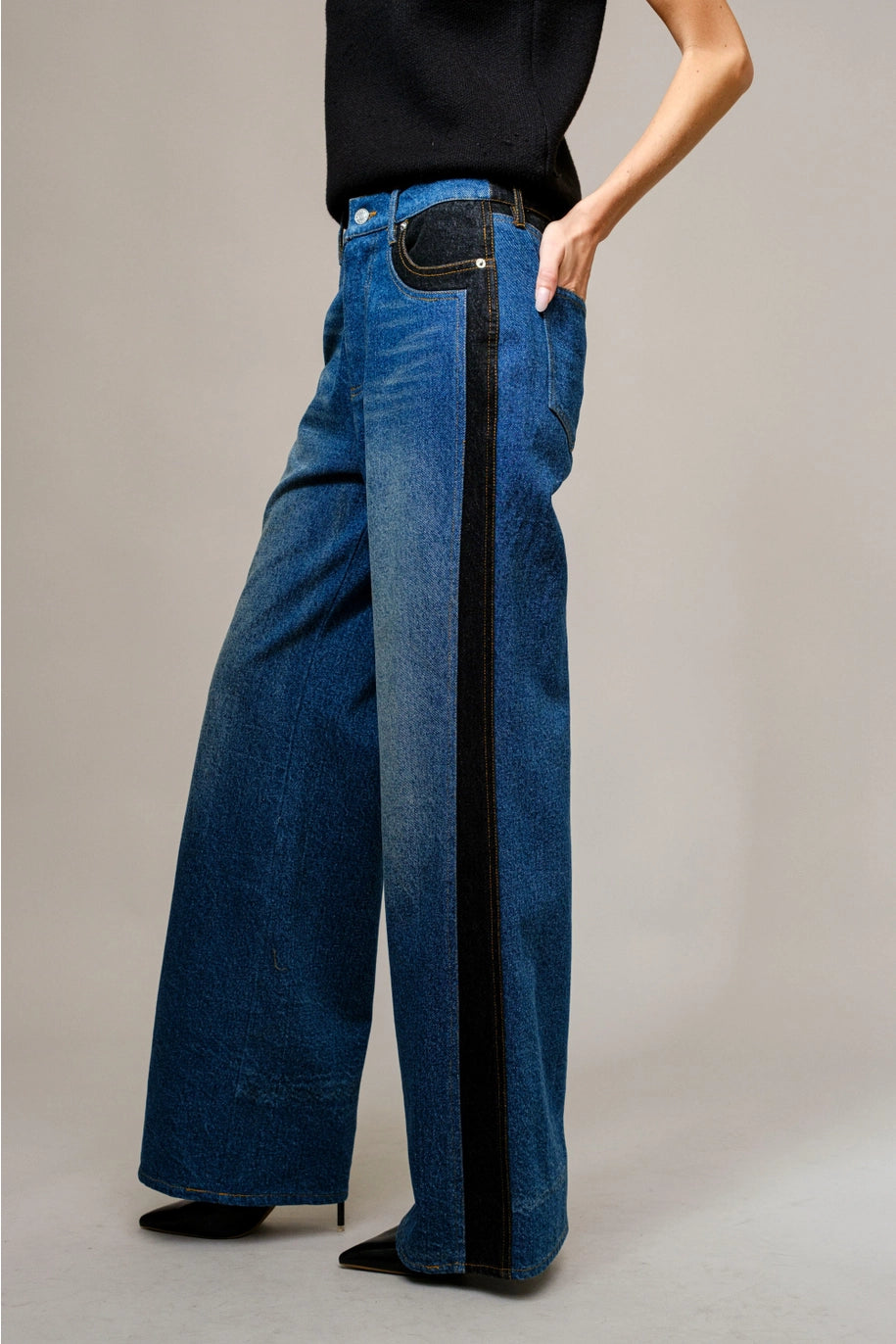 Person wearing wide-leg blue jeans with a black stripe on a neutral background