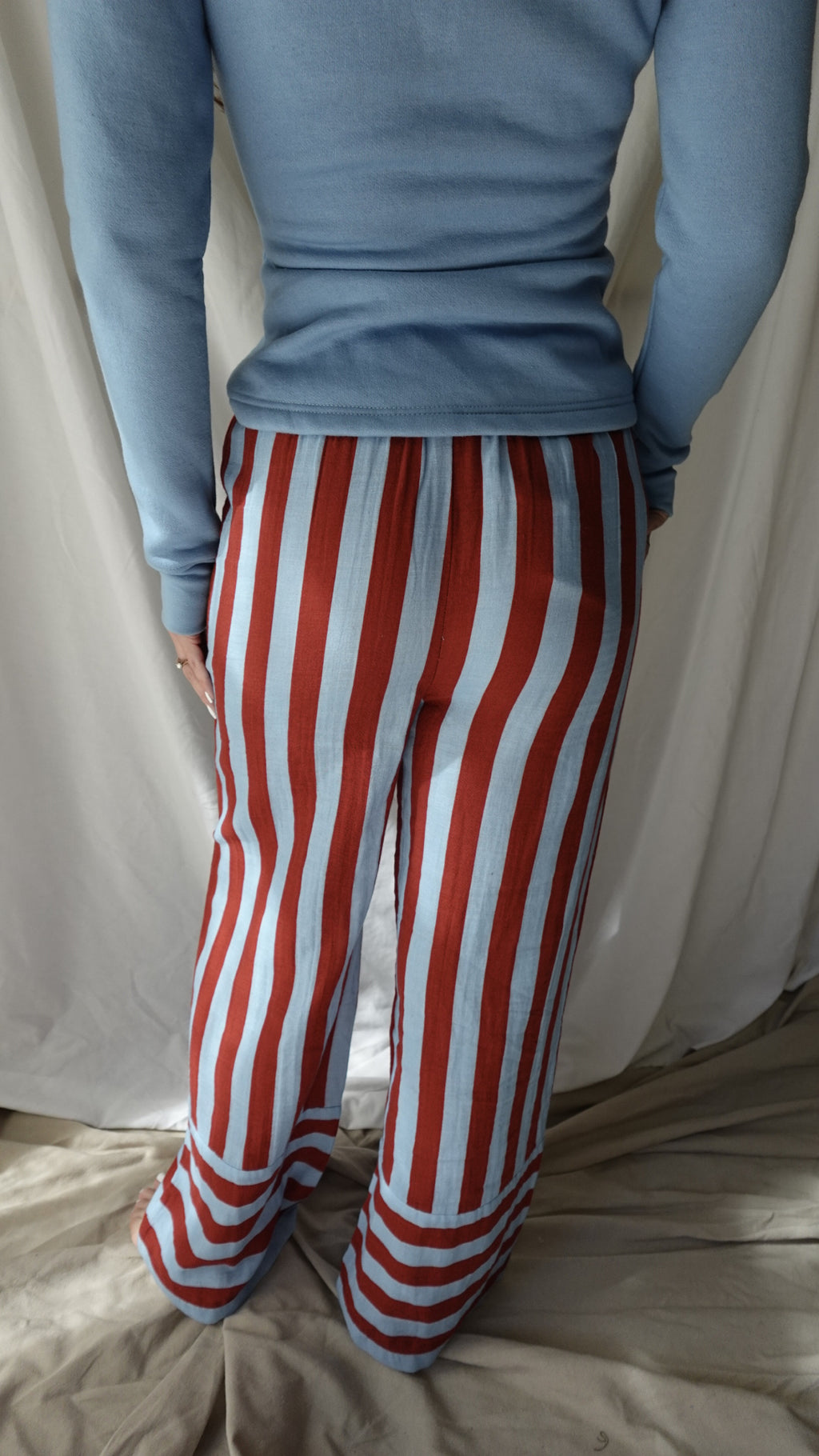 Person wearing blue gloves and red and white striped pants on a bed.
