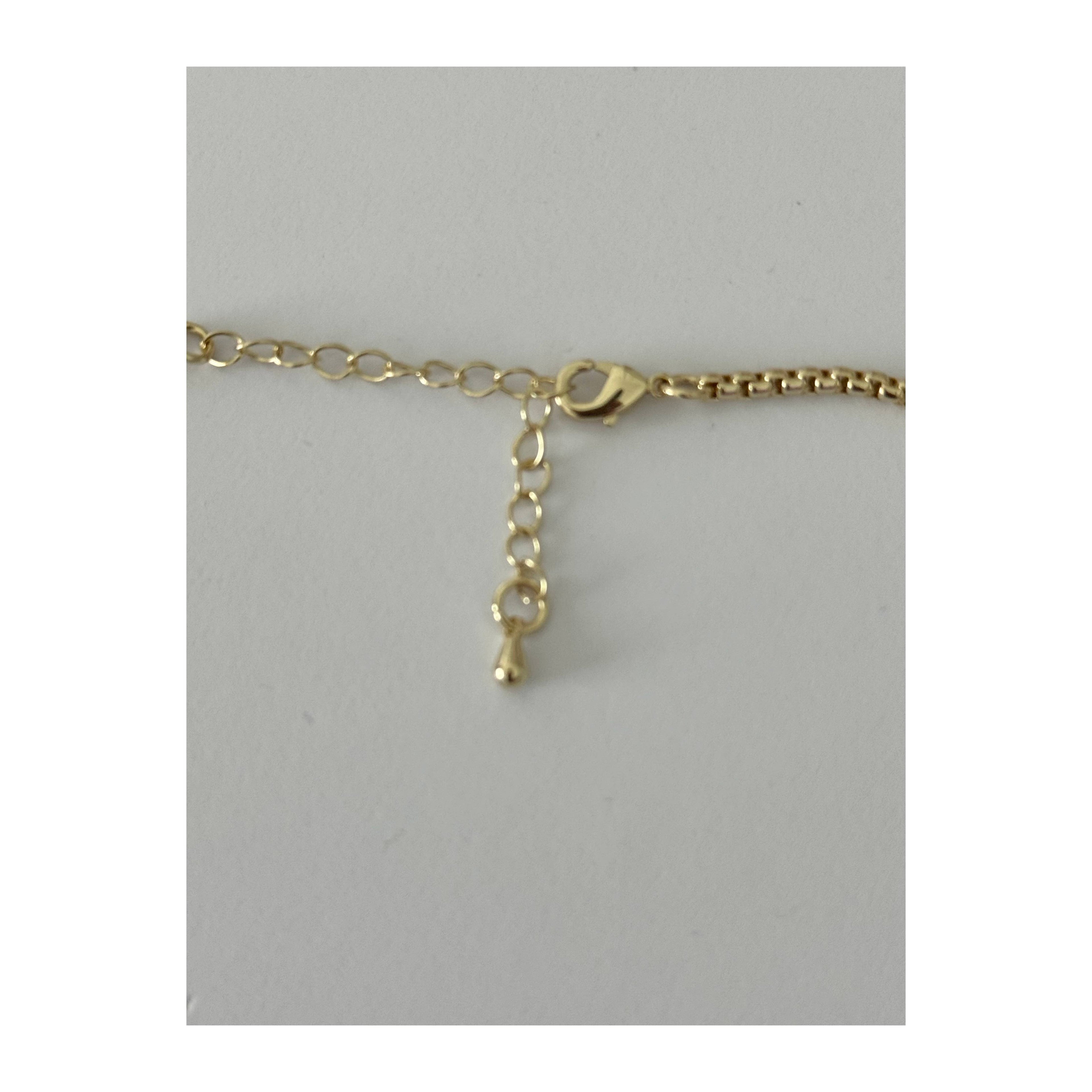 A close-up of a gold chain necklace showing a lobster clasp, extension chain, and a small key-shaped charm, set against a plain light gray background.
