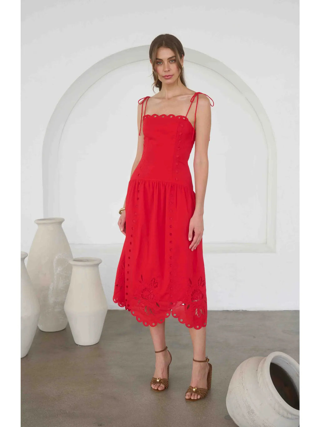 Woman wearing a red dress standing in front of white arches and vases.