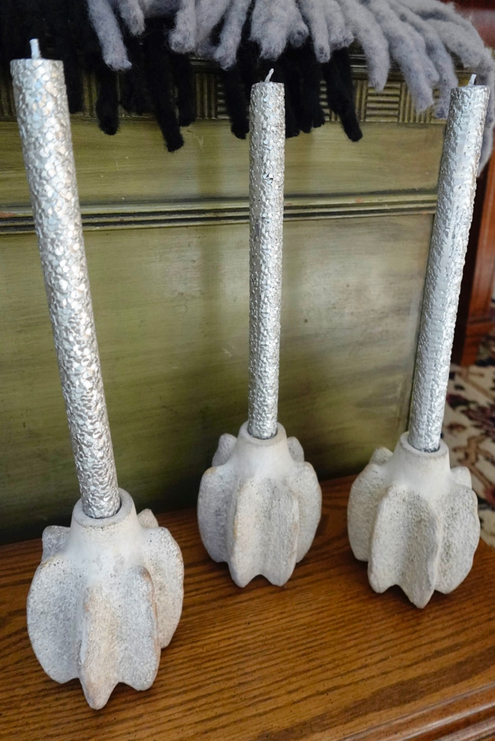 Three decorative candles with textured silver holders on a wooden surface.