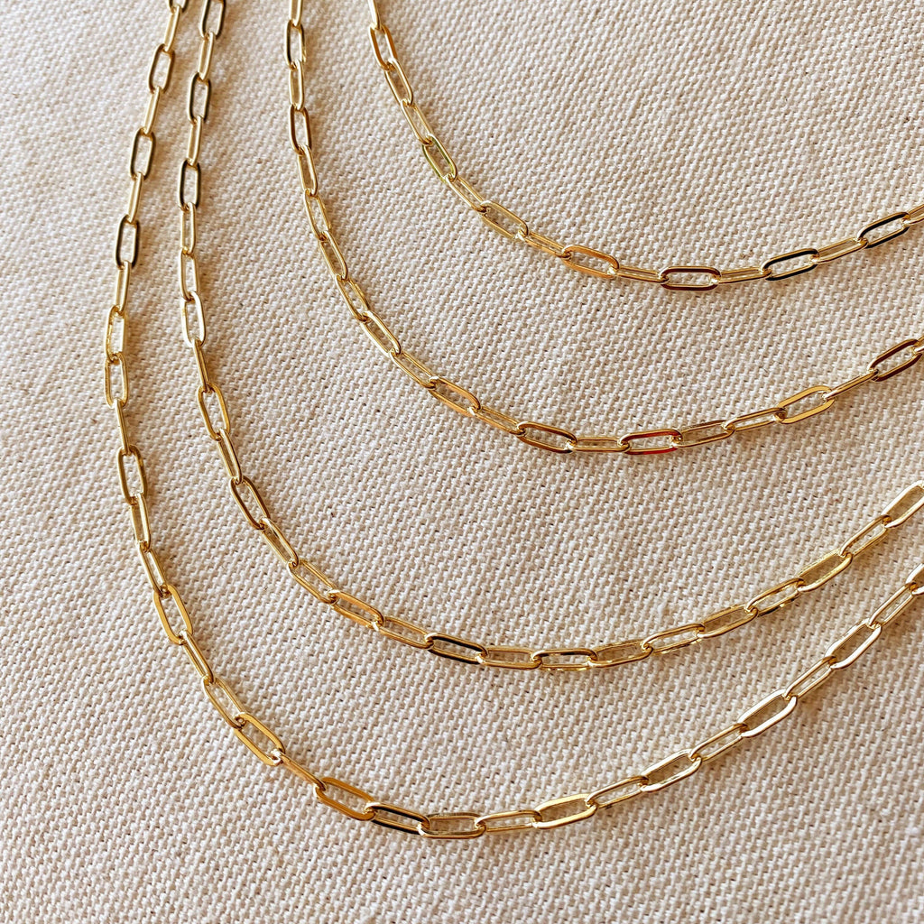 Three gold chain necklaces on a beige fabric background
