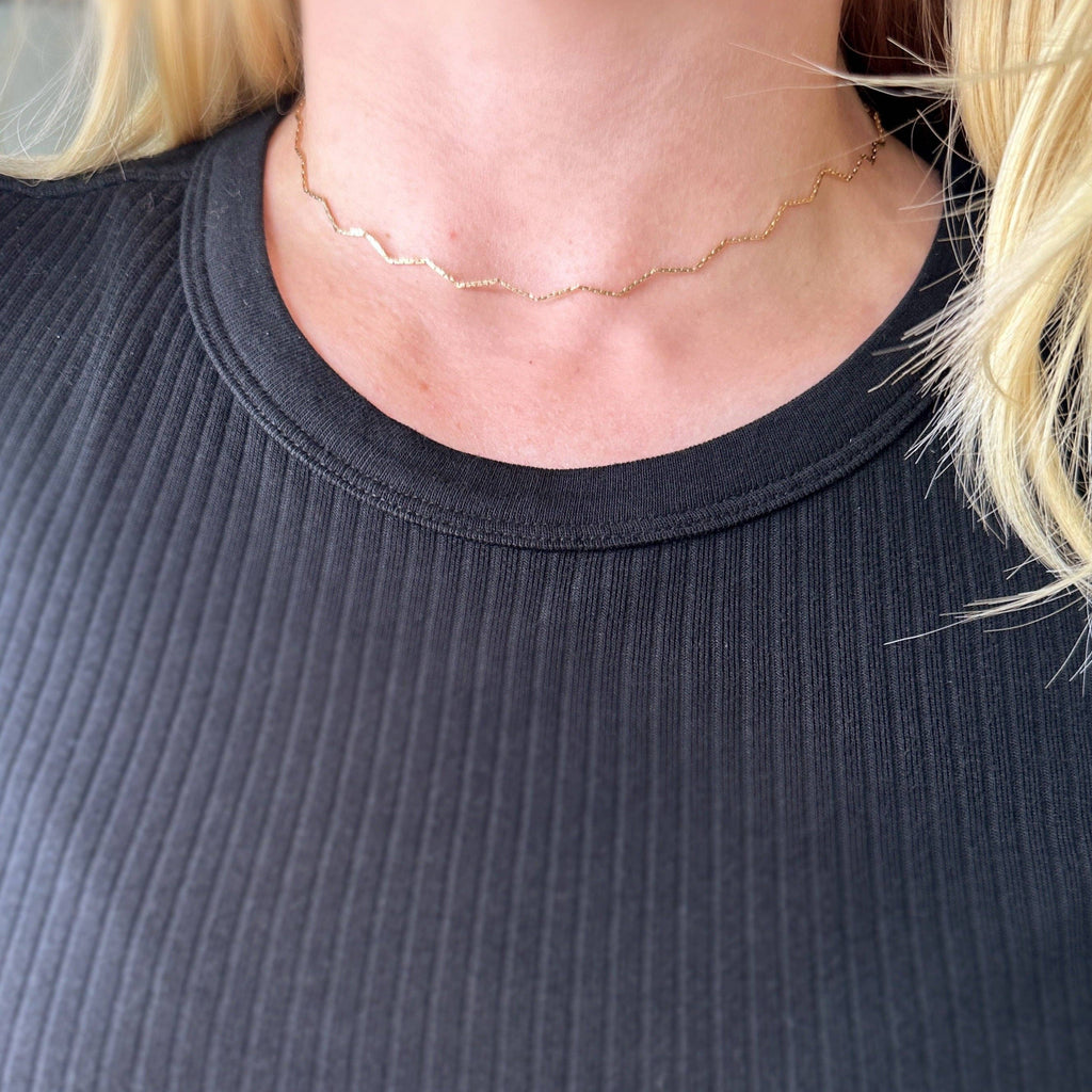 Person wearing a delicate gold necklace with a plain background