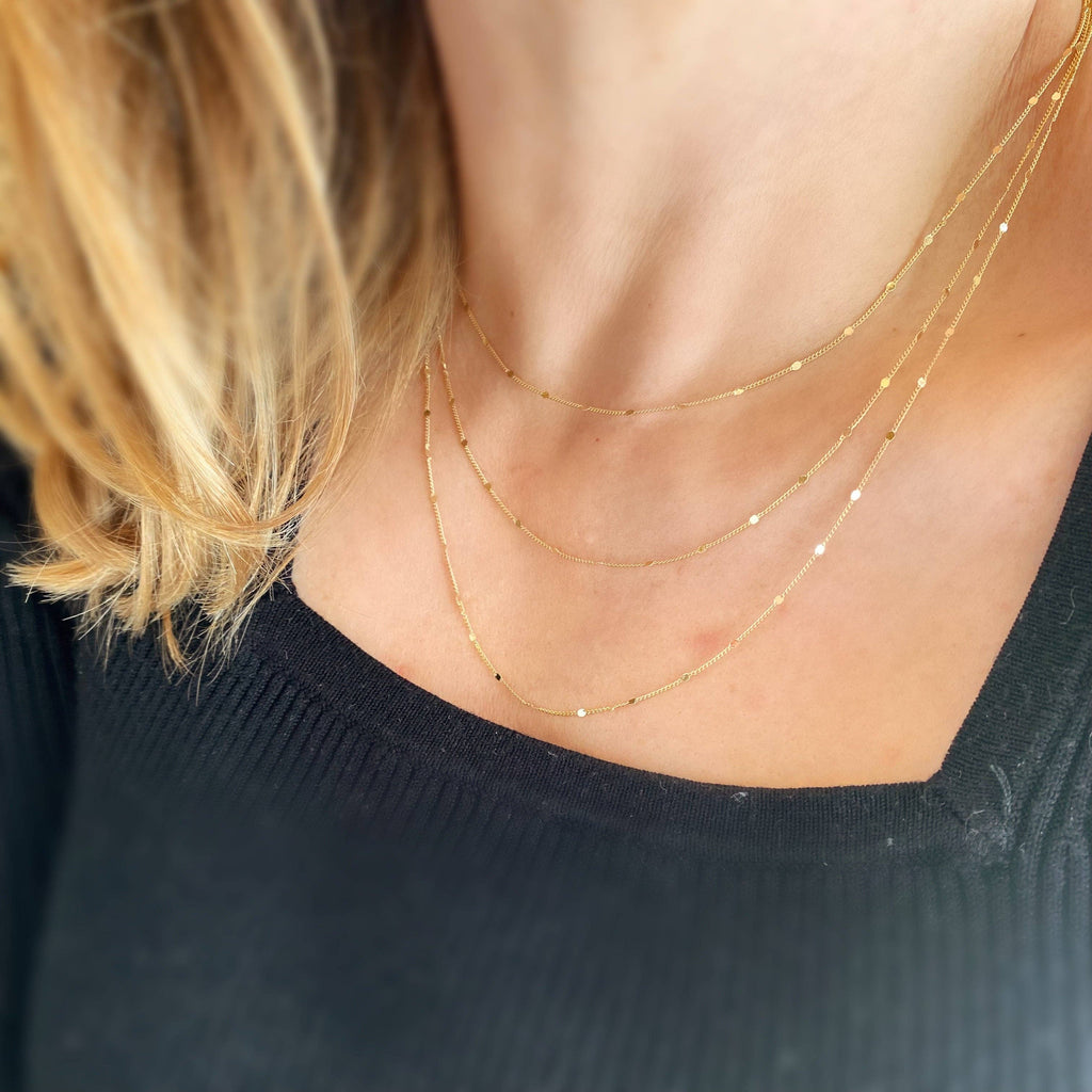 Close-up of a person wearing two gold necklaces with a blurred background