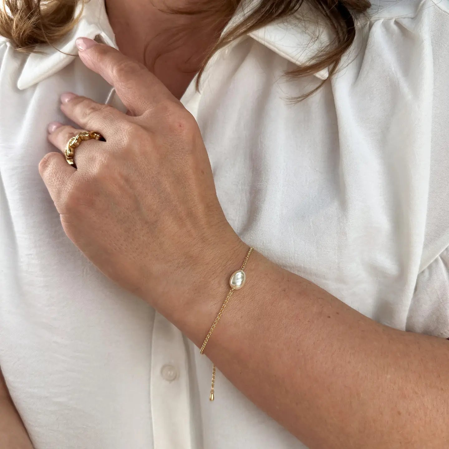 Close-up of a person wearing a gold ring and bracelet on a white shirt background