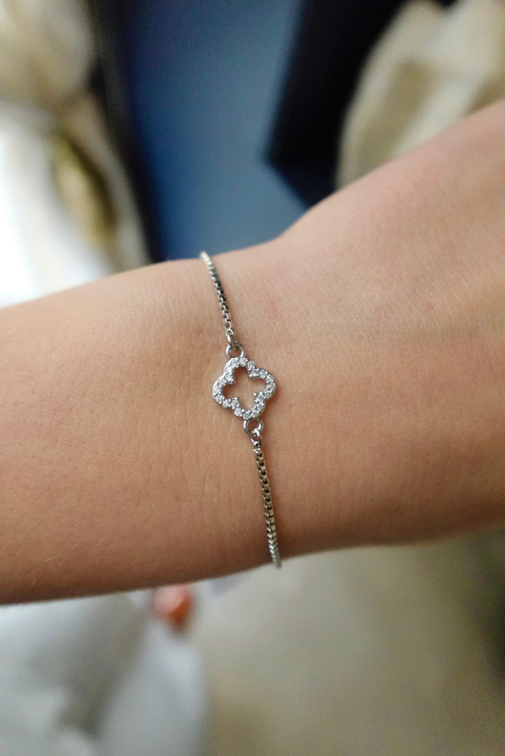 Silver bracelet with a clover-shaped charm on a wrist against a blurred background