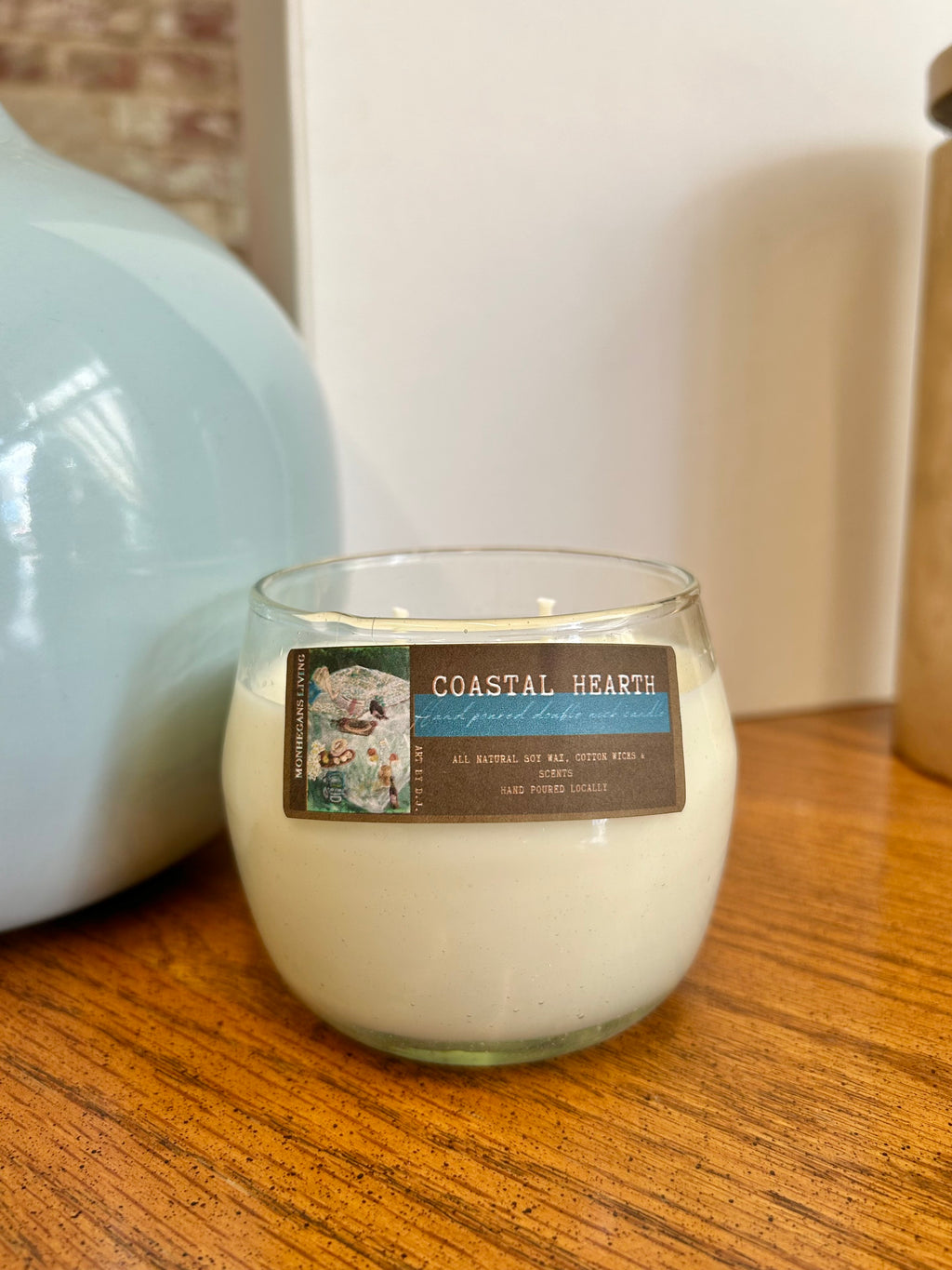 Glass candle labeled 'Coastal Hearth' on a wooden surface with a blurred background
