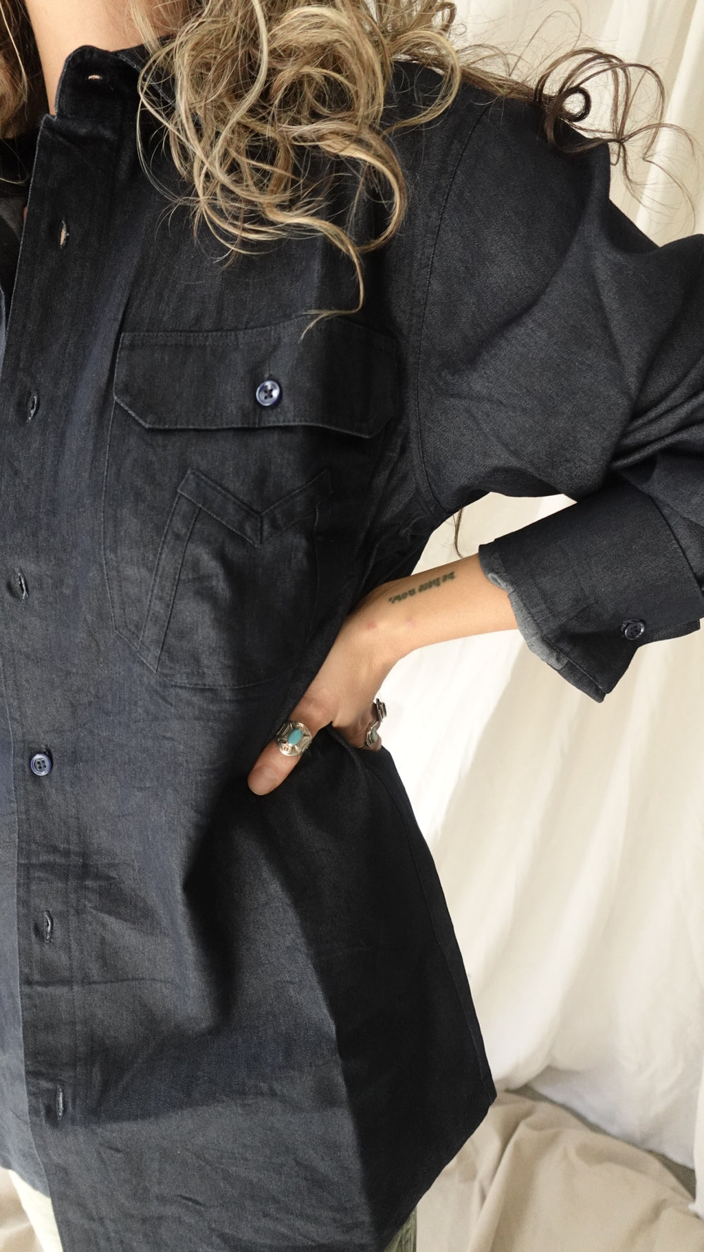 Person wearing a dark denim jacket with a close-up of the collar and buttons.