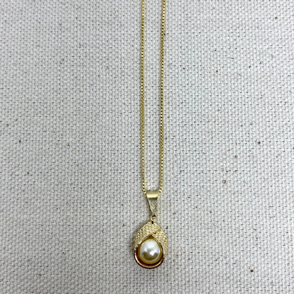 Gold necklace with a pearl pendant on a textured gray background